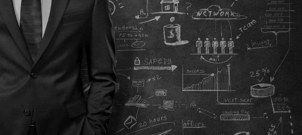 A businessman in a suit standing in front of a chalkboard.