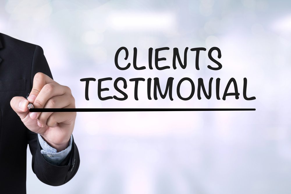 A person in a suit uses a marker to underline the words "Clients Testimonial" on a transparent surface.