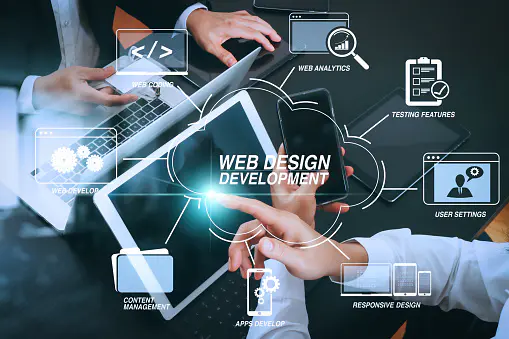 Two people work on tablets and laptops at a desk, with web design and development icons and terms digitally overlaid on the image.