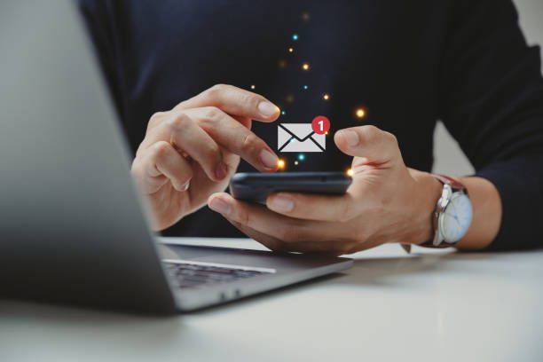 A person checks their smartphone for an email notification while sitting at a desk with a laptop.
