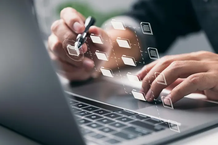 A person uses a laptop, interacting with floating digital folder icons, suggesting file management or data organization.