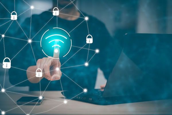 Person touches a virtual Wi-Fi icon on a screen, surrounded by padlock symbols, with a laptop and smartphone on the desk, representing secure wireless network connection.