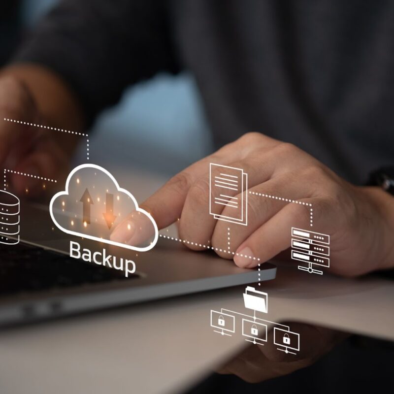 Hands typing on a laptop keyboard with virtual icons and the word "Backup" representing data backup and cloud storage technology.