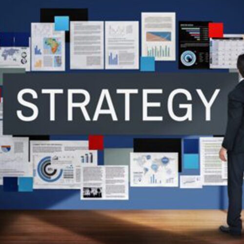 A person in business attire looks at a wall filled with documents, graphs, and charts, with a large sign reading "STRATEGY" in the center.
