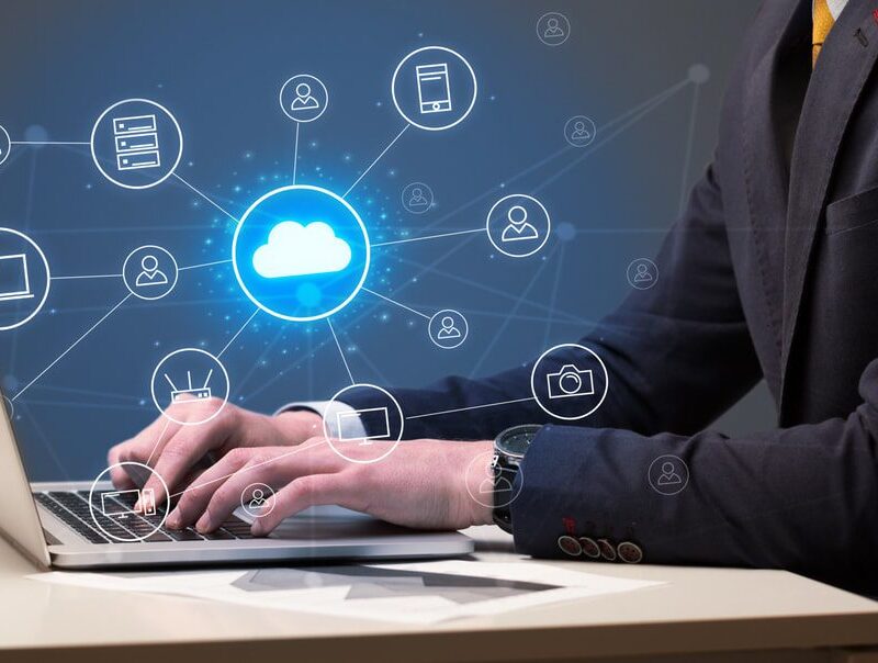 Person typing on a laptop with digital cloud computing icons and network connections overlayed on the image.