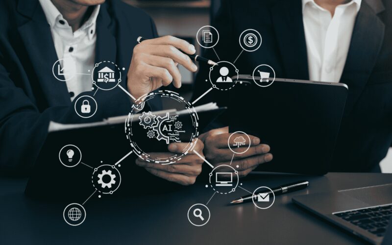 Two people in business attire review documents and a tablet, with digital graphics representing AI and technology icons overlayed in the foreground.
