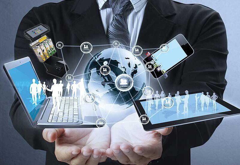 A person in a suit holds digital devices with holographic images of people, a globe, and network icons, symbolizing global digital connectivity and technology.