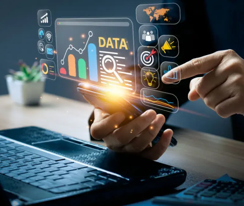 A person uses a smartphone near a laptop, interacting with floating data analytics graphics and digital icons representing charts, targets, and global connections.