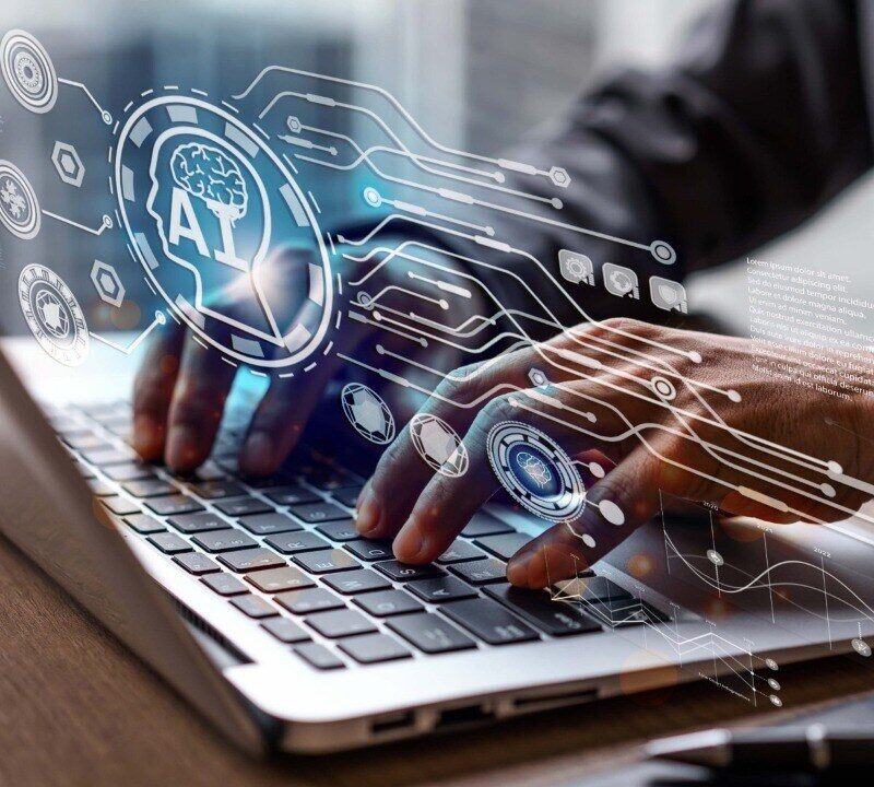 Person typing on a laptop with digital graphics of AI and technology icons overlaying the image, symbolizing artificial intelligence and data processing.