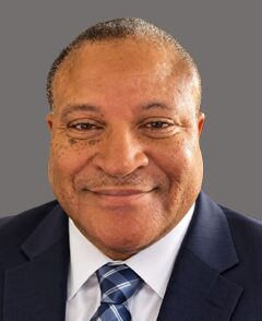 Headshot of a smiling man wearing a navy blue suit and a patterned blue tie.