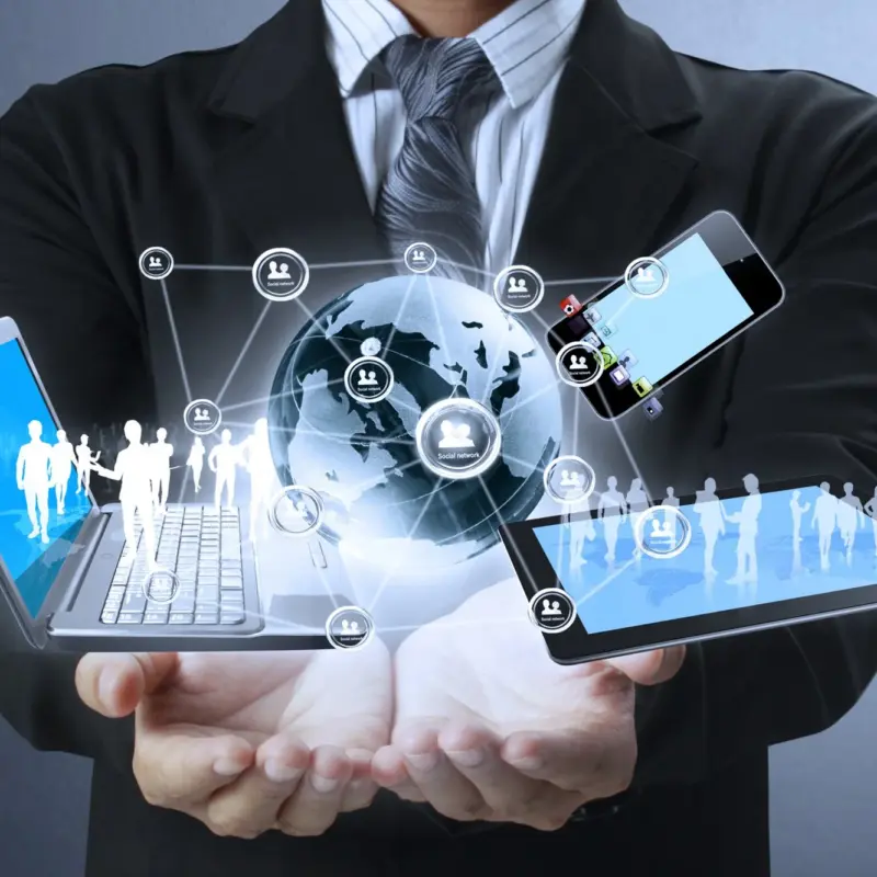 A person in a suit holding a globe, a laptop, a tablet, and a smartphone, all connected by digital social network icons.