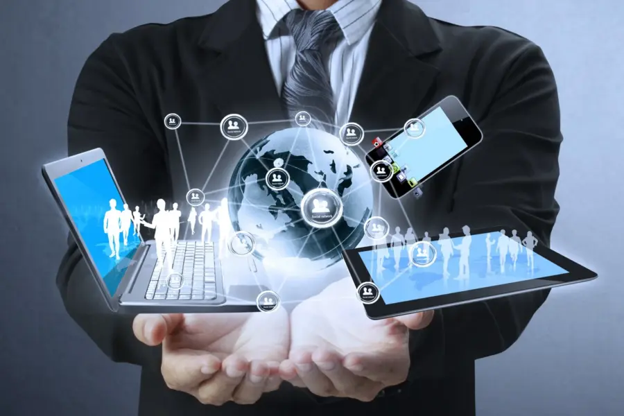 A person in a suit holding a globe, a laptop, a tablet, and a smartphone, all connected by digital social network icons.