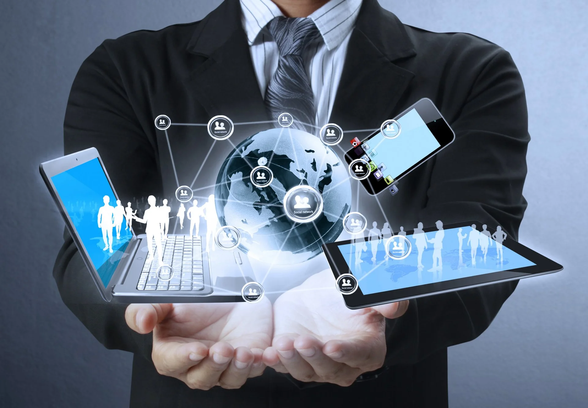 A person in a suit holding a globe, a laptop, a tablet, and a smartphone, all connected by digital social network icons.